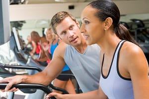 Personal Trainer Encouraging Woman Using Treadmill At Gym