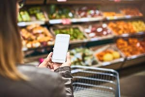 Save paper, use a grocery list app. a woman using a mobile phone in a grocery store. Save paper, use a grocery list app.