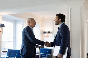 Two businessmen standing indoors, shaking hands.