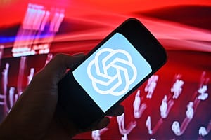 Hand shows a smartphone with the ChatGPT logo in front of a red background