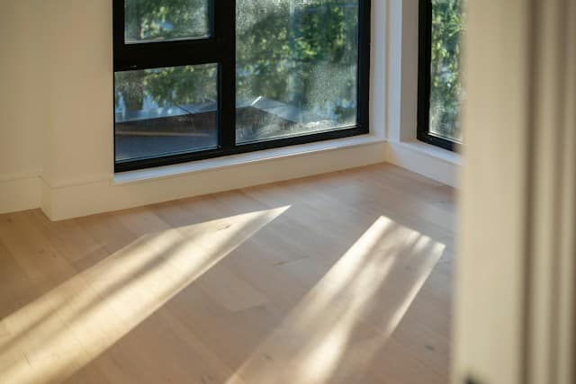 Sunlight casting long shadows across light wooden floorboards in a room with large windows