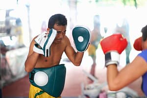 Mature woman practicing boxing with male trainer in gym