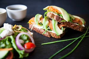 Smoked fish and avocado open sandwiches with salad and dipping sauces on slate