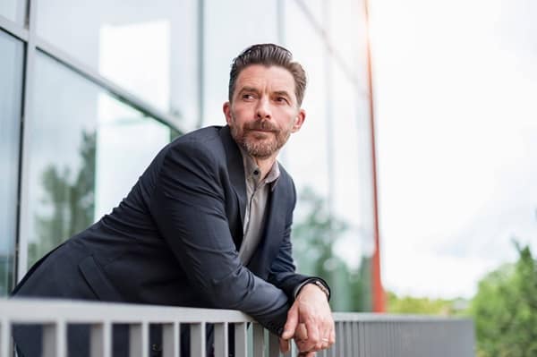Mature businessman leaning on office handrail looking over his shoulder