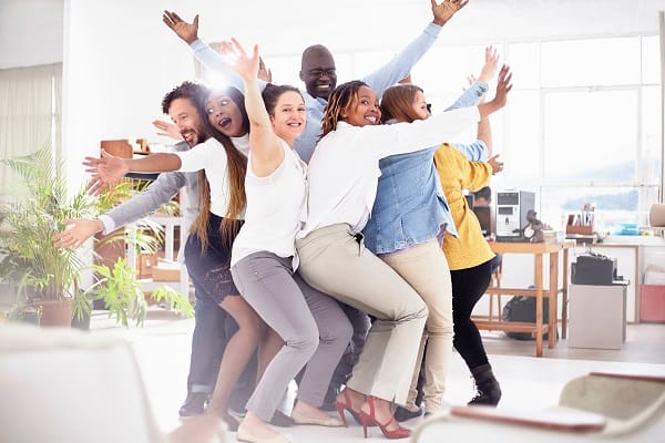 Colleagues in huddle, arms raised looking at camera smiling