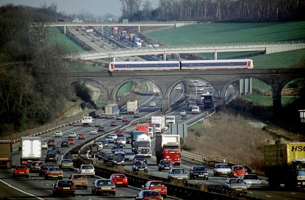 A Chiltern Trains DMU glides gracefully over the congested traffic on the M25 motorway. C1993.