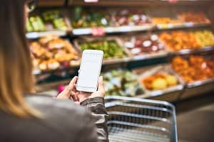 Save paper, use a grocery list app. a woman using a mobile phone in a grocery store. Save paper, use a grocery list app.