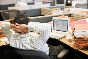 Businessman in cubicle with laptop and stacks of files