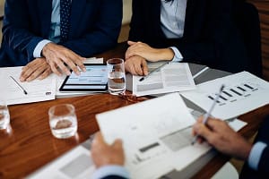 Businessmen and woman at boardroom table using digital tablet and working on paperwork, cropped