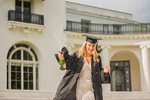 Graduating student with opened bottle of champagne at campus