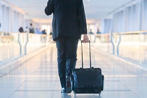Businessman walking and wheeling a trolley suitcase at the lobby, talking on a mobile phone. Business travel concept. Re