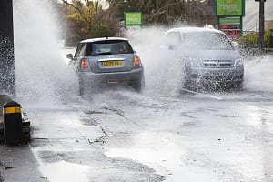 Motorists driving too fast through large puddles soaking pedestrians and property in Ambleside, Cumbria, UK.