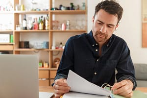 Man with laptop looking at paperwork